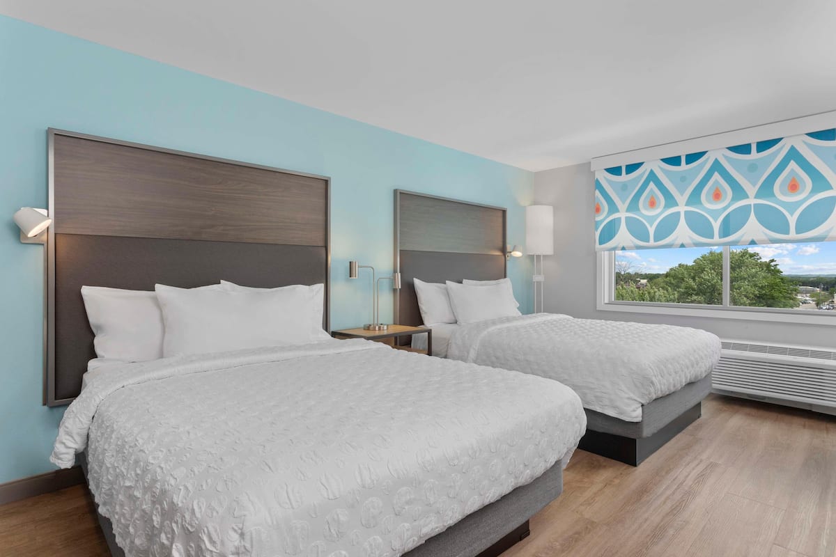 Una habitació d'hotel amb dos llits, un gran finestral i una cortina estampada.