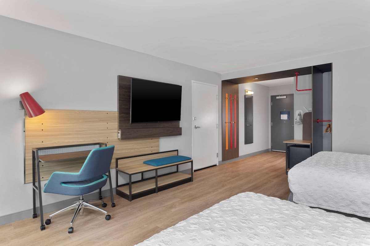 Habitació d'hotel amb un llit, un escriptori amb cadira, una televisió penjada a la paret i una porta que dona a una altra habitació.
