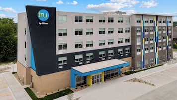 Un hôtel moderne, reconnaissable à son enseigne « tru by Hilton » bien visible, avec de nombreux étages et un espace d’entrée abrité.