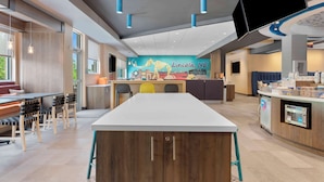 A modern restaurant with a long counter, wooden chairs, and a mural of a dinosaur.