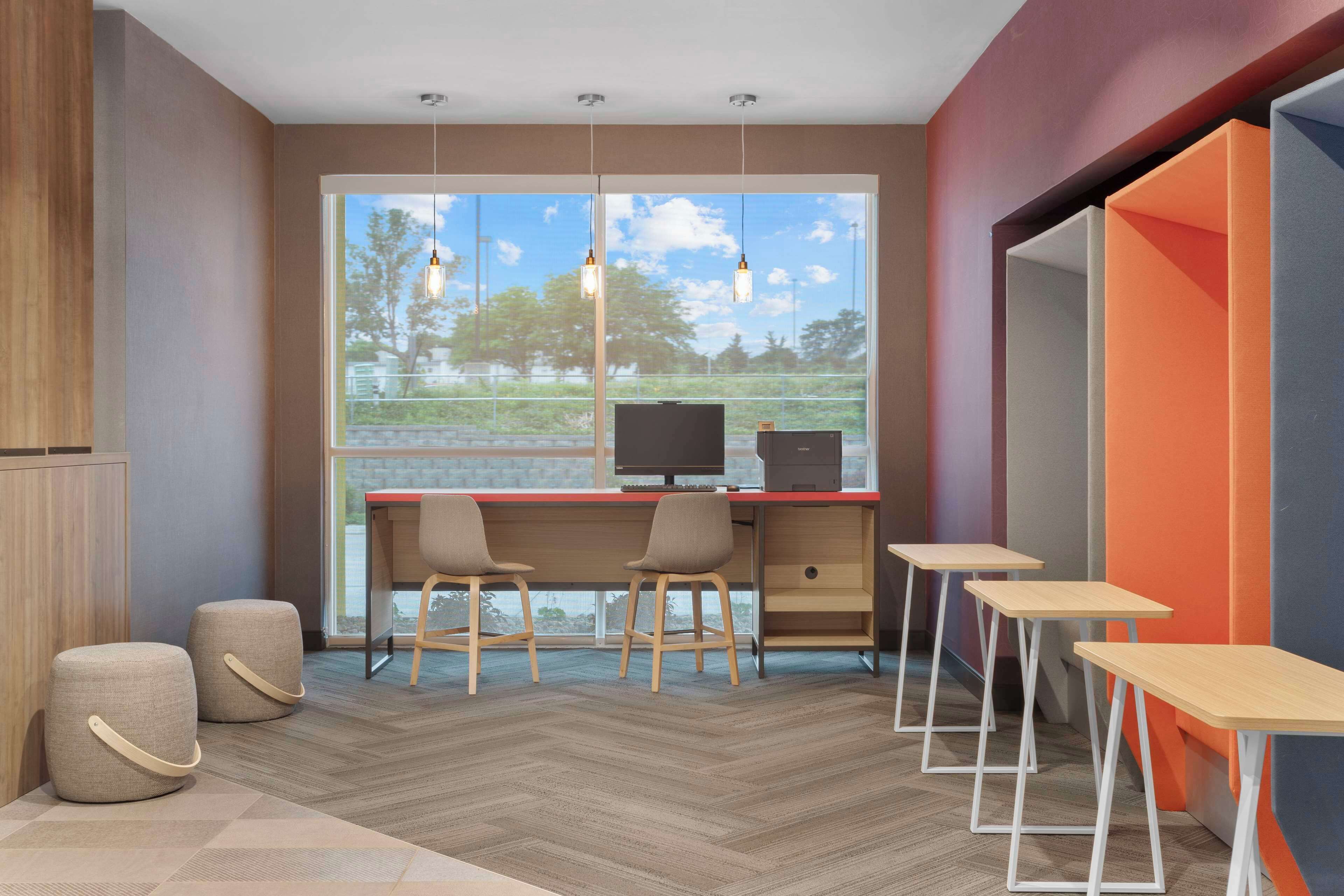A modern office space with a large window, two desks, two chairs, and a small table.