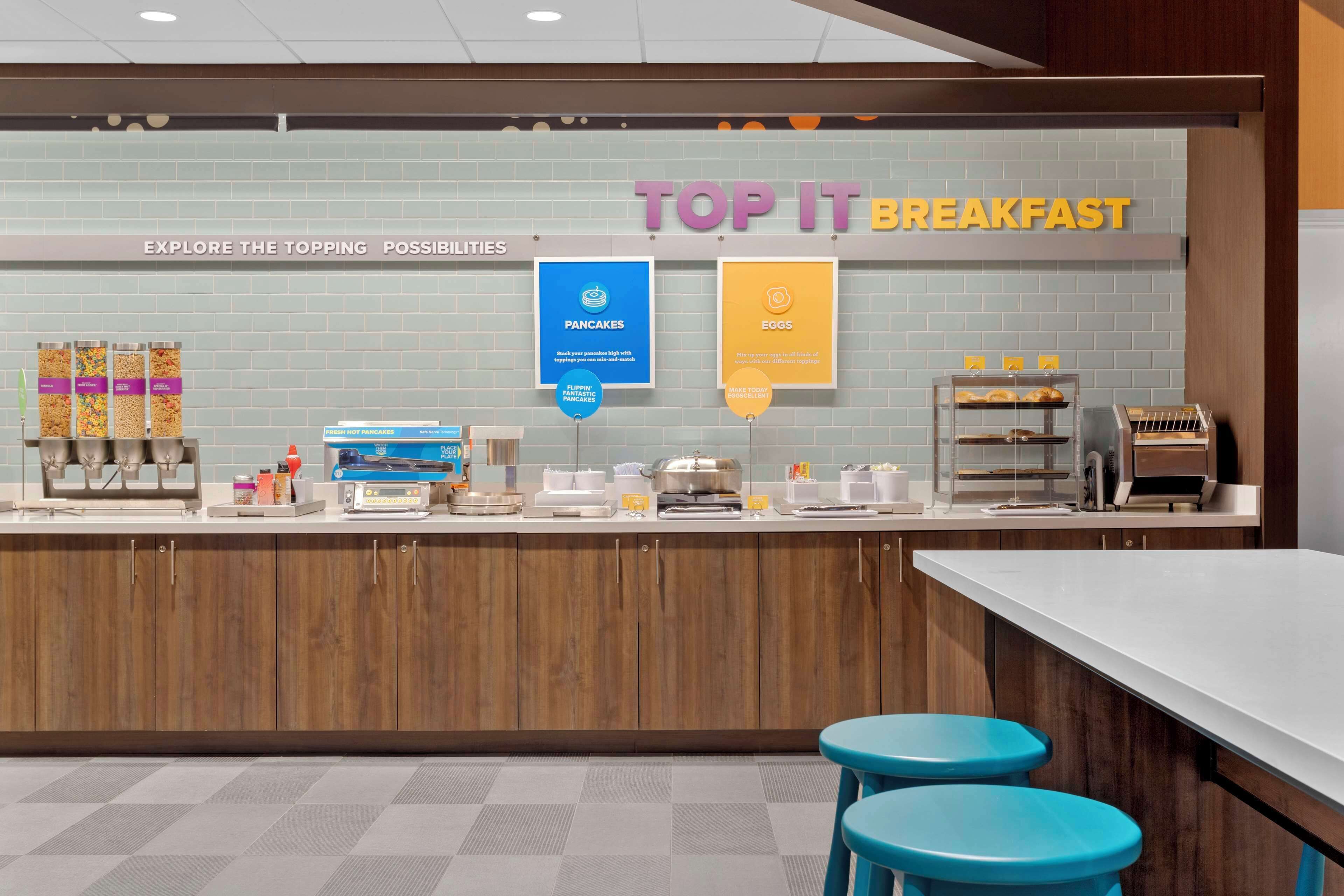 Ein Frühstücksbuffet mit einem Schild, auf dem 'TOP IT BREAKFAST' steht, und Bereichen mit der Aufschrift 'PANCAKES' und 'EGGS'.