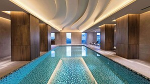 A modern indoor swimming pool with a tiled floor, wooden panel walls, and a view of the city through large windows. - DoubleTree by Hilton Osaka Castle (Osaka)