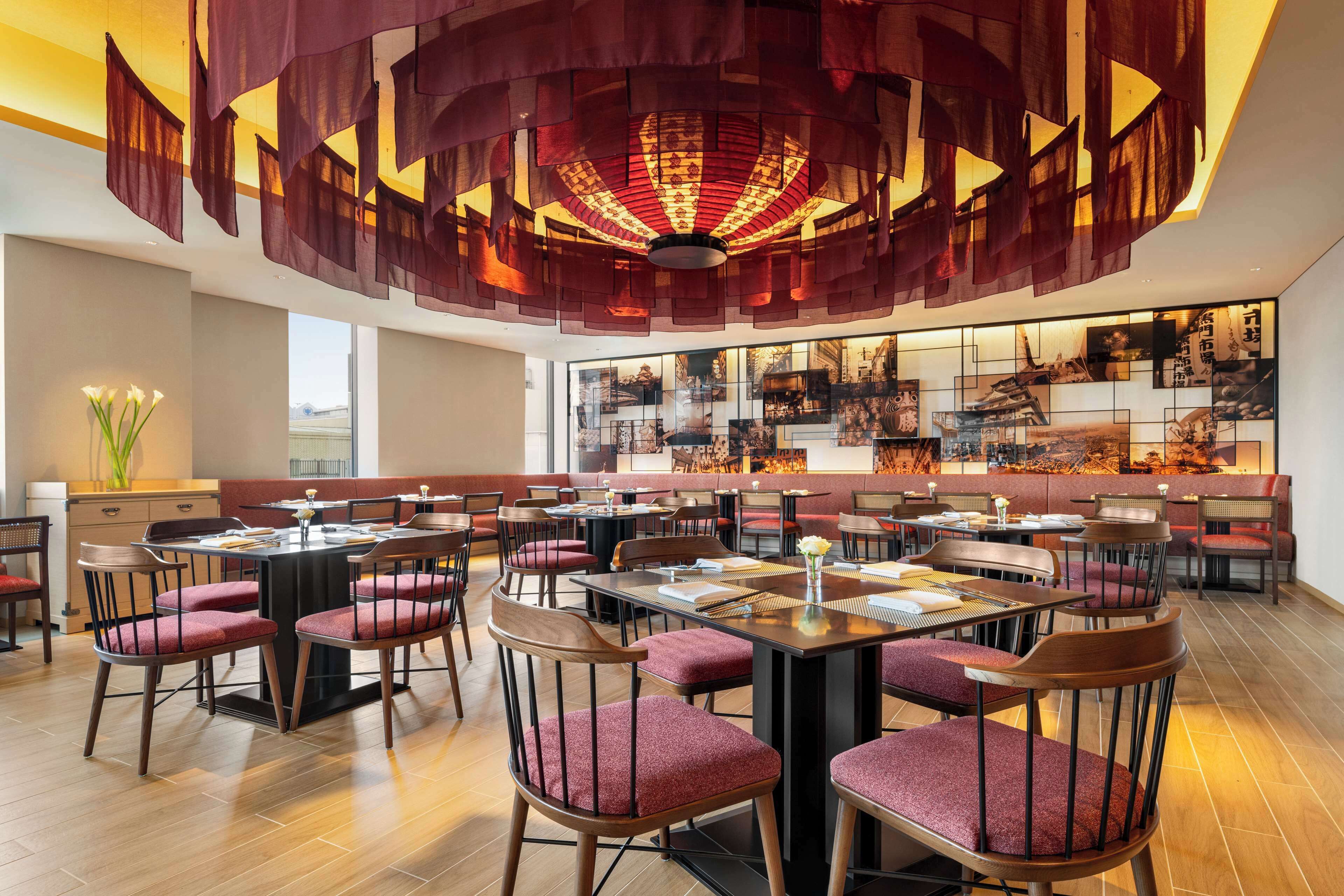 Un restaurante espacioso con numerosas mesas y sillas, un moderno candelabro y una pared decorada con obras de arte enmarcadas.