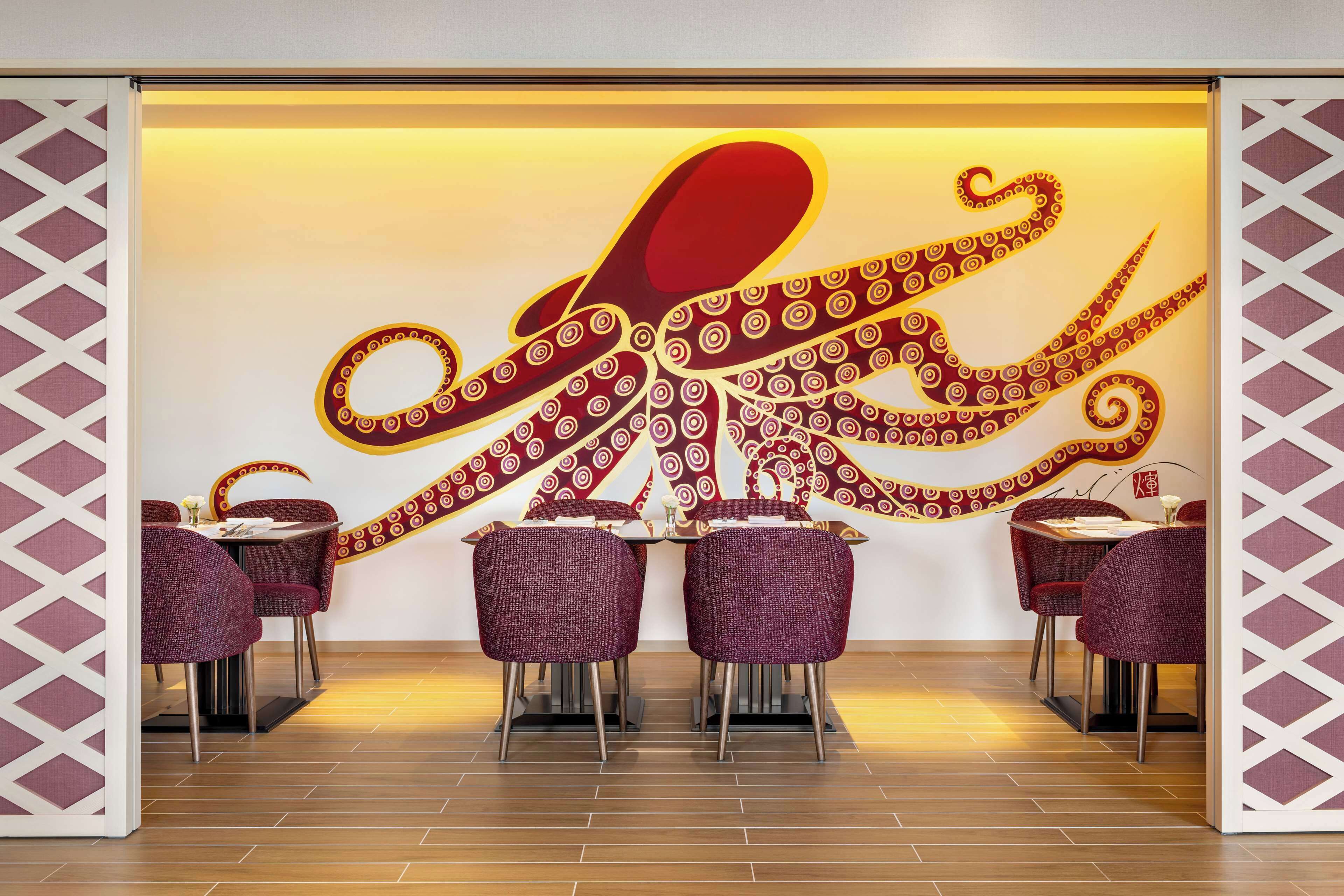 A restaurant with a large octopus mural on the wall, purple upholstered chairs, and a wooden floor.