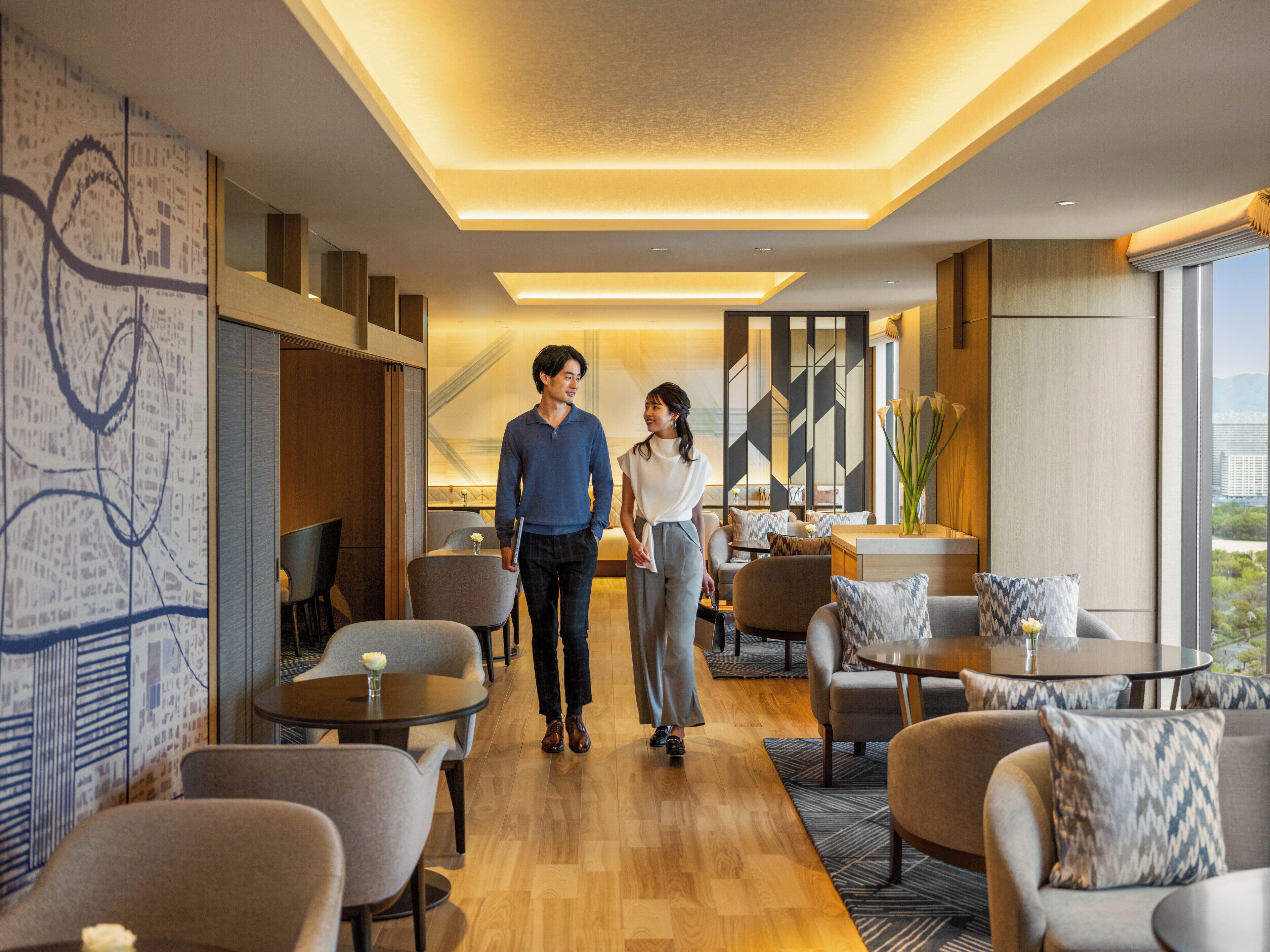 Un hall d’hôtel moderne avec un plancher en bois, des coins salon et une grande fenêtre donnant sur la ville.