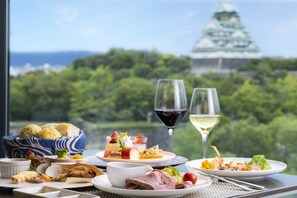 Une table dressée avec divers plats et deux verres de vin, offrant une vue sur un paysage verdoyant et luxuriant ainsi que sur un bâtiment traditionnel.
