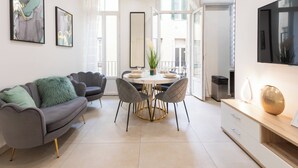 Un salon moderne avec un canapé gris, une table à manger avec des chaises et un téléviseur fixé au mur.