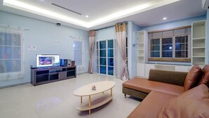 Ein modernes Wohnzimmer mit Flachbildfernseher, einer Couch, einem Couchtisch und einem Fenster mit Jalousien.