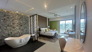A modern hotel room with a large bed, a separate bathroom with a bathtub, a desk, and a view of the city. - Garza Blanca Resort & Spa - LUXURIOUS 3 BDRM Penthouse Loft, & Private Jacuzzi (Cancún)