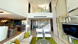 A spacious living area with a sofa, chairs, a TV, and a kitchen in the background. - Garza Blanca Resort & Spa - LUXURIOUS 3 BDRM Penthouse Loft, & Private Jacuzzi (Cancún)