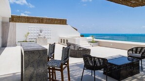 A rooftop terrace with outdoor seating, a stone wall, and a view of the ocean. - Garza Blanca Resort & Spa - LUXURIOUS 3 BDRM Penthouse Loft, & Private Jacuzzi (Cancún)