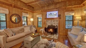 A cozy cabin interior with a stone fireplace, wooden walls, and a comfortable seating area. - The Cabin @ Possum Trot- A Rustic Chic Escape (Clayton)