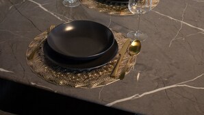 Een eettafel met zwarte borden, gouden bestek en heldere wijnglazen.