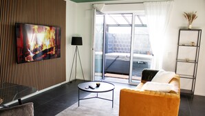 Een moderne woonkamer met een televisie, een ronde salontafel, een bank en een schuifdeur naar een buitengebied.