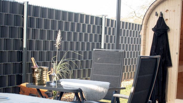 Een jacuzzi met glazen omheining, een houten terras en een omheinde achtertuin.