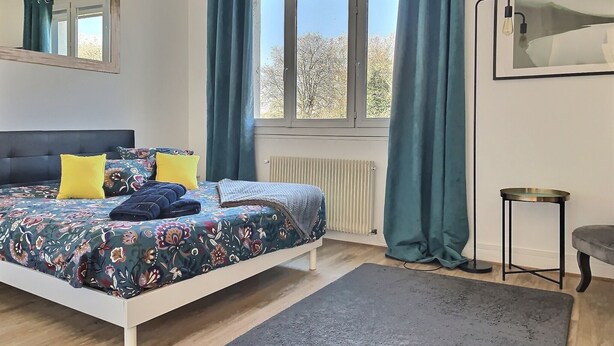 Ein Schlafzimmer mit einem Bett, einem Fenster mit Vorhängen, einem Heizkörper und einem kleinen Tisch.