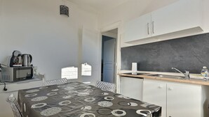 Eine kleine Küche mit Mikrowelle, Wasserkocher und Spüle. Ein Esstisch mit gemustertem Tischläufer steht bereit.