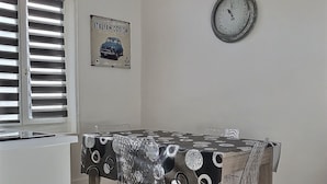 Ein Essbereich mit einem Tisch, der mit einer schwarz-weiß gemusterten Tischdecke bedeckt ist, einer Uhr an der Wand und einem Poster, das Vintage-italienisches Design bewirbt.