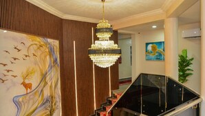 A grand staircase with a red carpet, a chandelier, and a large wall painting.