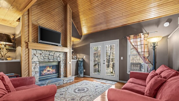 A cozy living room with a stone fireplace, red sofas, and a large window with a view of the outdoors.