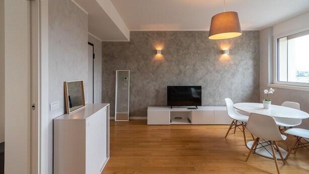 A modern living room with a flat-screen TV, a dining table with chairs, and a pendant light.