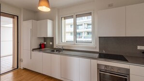 A modern kitchen with white cabinets, a stainless steel sink, and a window overlooking a balcony.