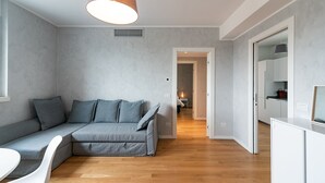 A modern living room with a grey sectional sofa, a white dining table, and a kitchen area in the background.
