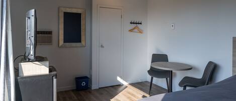 A compact hotel room with a bed, a small table with two chairs, a television, a mirror, and a door.