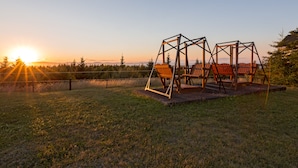 A wooden swing set in a grassy field with a sunset in the background.