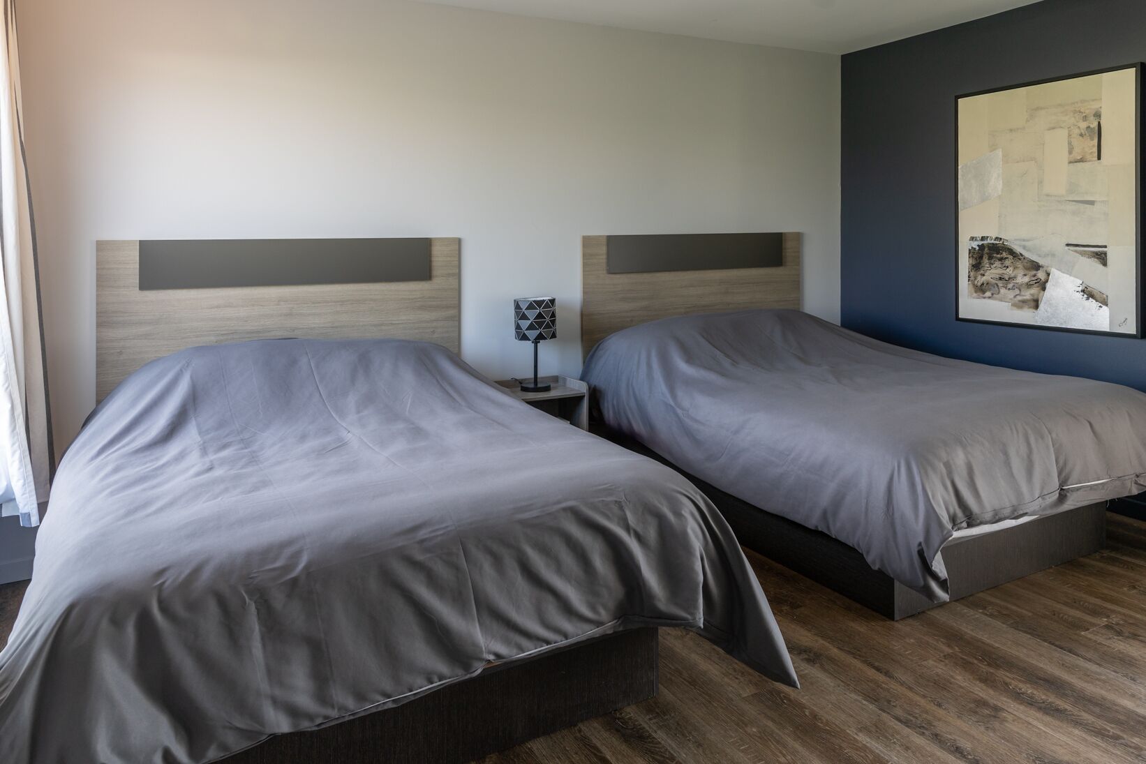 Une chambre d’hôtel avec deux lits, une table de chevet avec une lampe et un grand tableau abstrait accroché au mur.