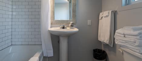 A bathroom with a white pedestal sink, a mirror, a bathtub, and a toilet.