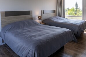 A hotel room with two beds, a nightstand with a lamp, and a large window with a view of trees. - Le Fraser Motel (Rivière-du-Loup)