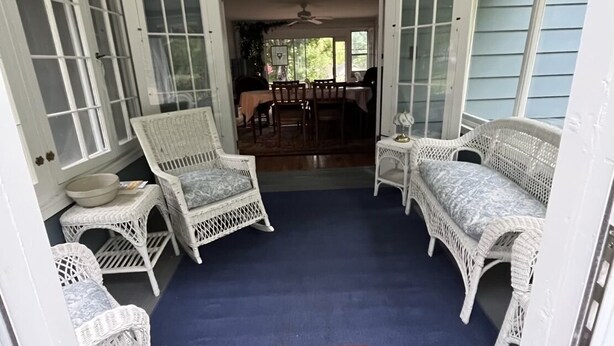En inglasad veranda med vita möbler i rotting, en blå matta och en röd och beige trasmatta.