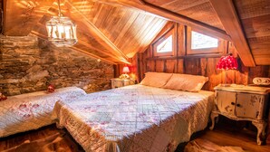 A cozy attic bedroom with a stone wall, wooden ceiling, a large bed with floral bedding, a nightstand, and a hanging light fixture. - 1 Bedroom Cabin in Isola (Isola)