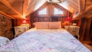 A cozy attic bedroom with a large bed, wooden beams, stone wall, and a skylight. - 1 Bedroom Cabin in Isola (Isola)
