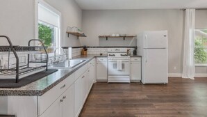 Una cocina moderna con armarios blancos, encimera de granito, pileta de acero inoxidable, horno empotrado y refrigerador blanco.