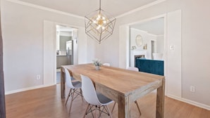 A dining area with a wooden table, white chairs, and a geometric pendant light. - Tulsa Vintage Chic Cottage |King Bed •Expo•TU•Dtwn (Tulsa)
