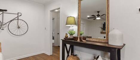 Un couloir avec un vélo accroché au mur, une console sur laquelle sont posés une lampe, un miroir et un ventilateur de plafond.