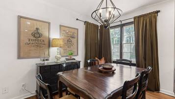 Een eetkamer met een houten tafel, stoelen, een kroonluchter en gordijnen.