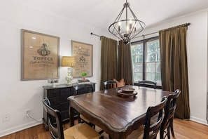 Uma sala de jantar com mesa de madeira, cadeiras, um candelabro e cortinas.