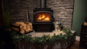 Een houtkachel tegen een achtergrond van een stenen muur, een metalen emmer en een stapel hout.