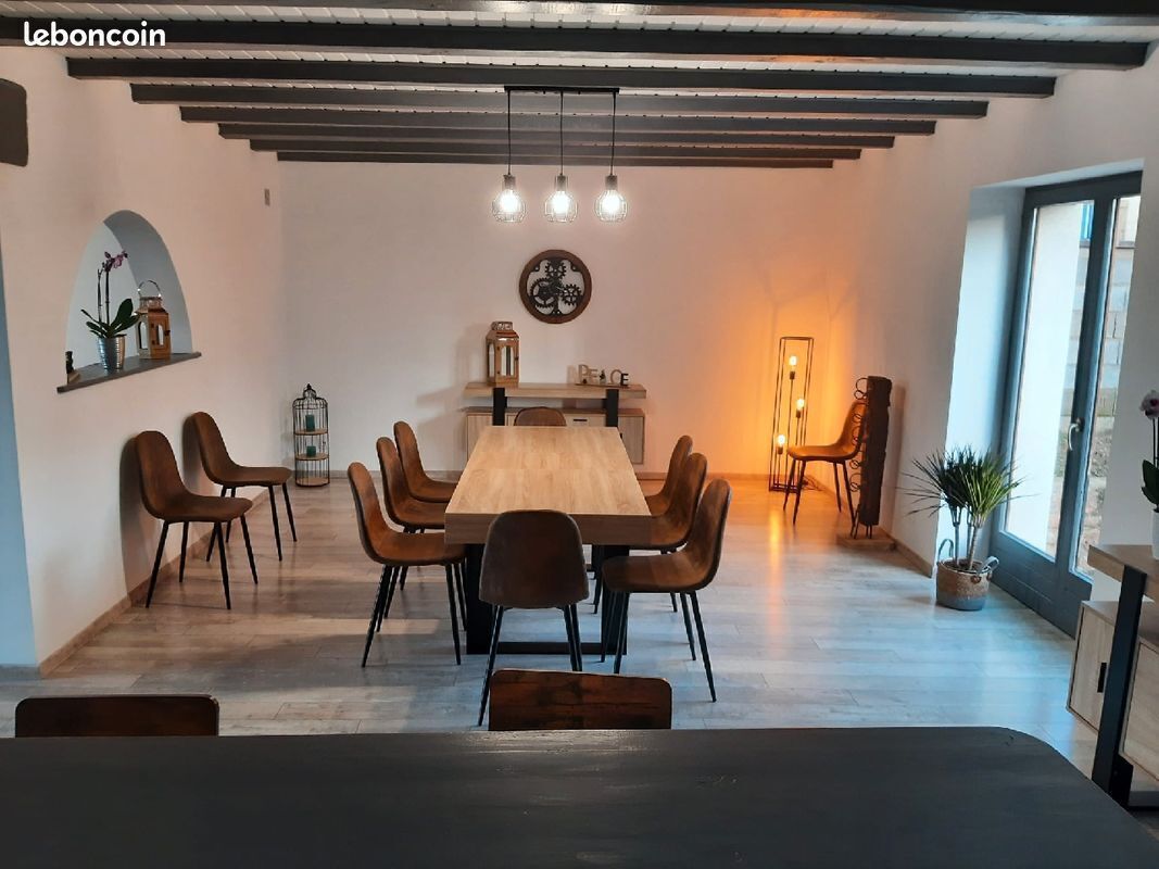 Un espace repas avec une longue table en bois entourée de chaises, un luminaire suspendu et un élément décoratif mural.