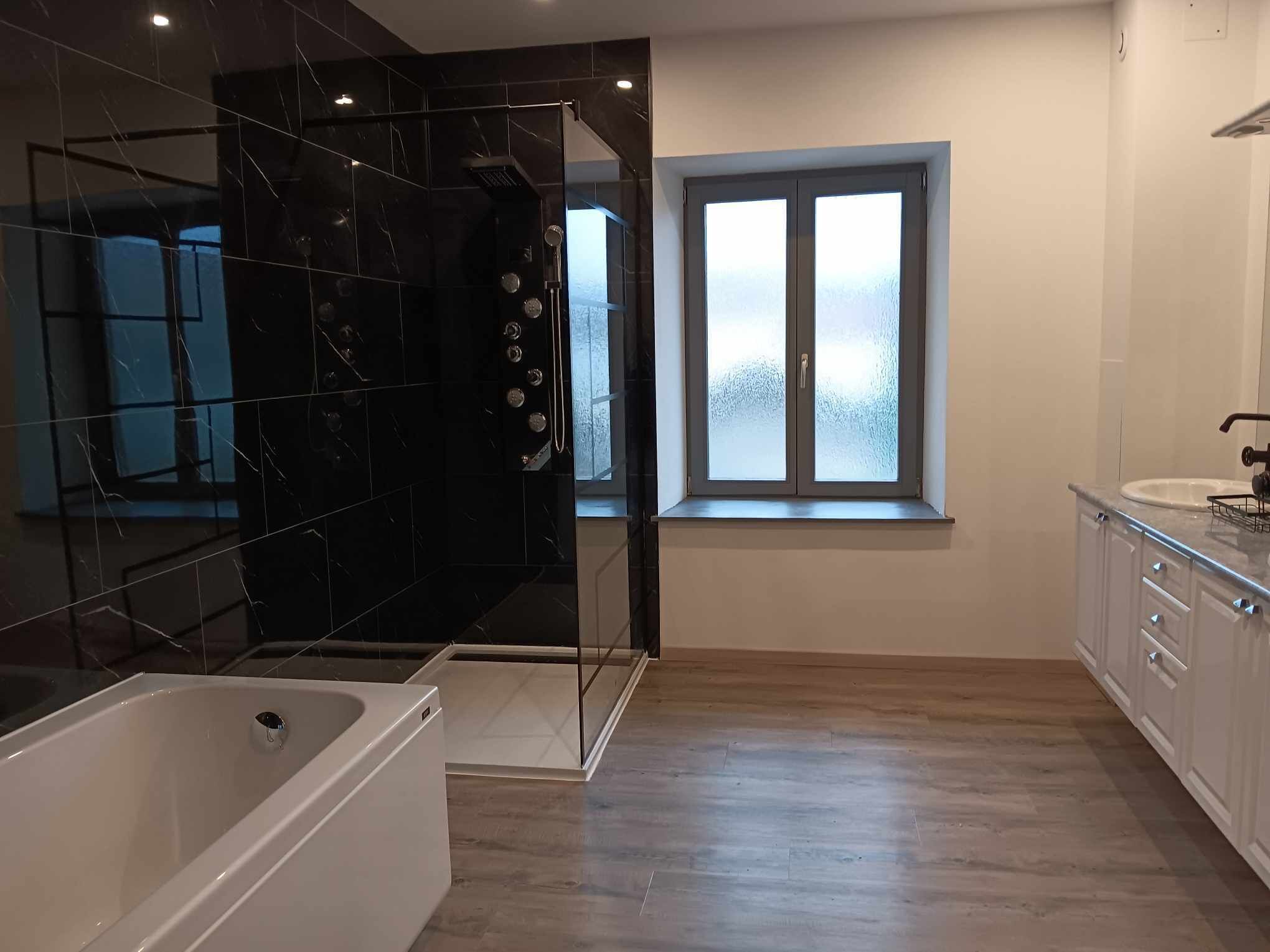 A modern bathroom with a bathtub, a glass shower enclosure, and a window with frosted glass.