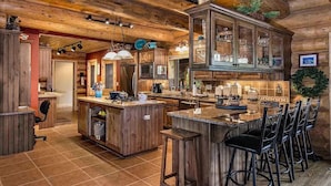 Une cuisine rustique avec des meubles en bois, un îlot central doté de tabourets de bar et un grand plafond en bois.