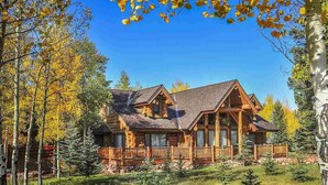 Une cabane en rondins avec des fondations en pierre, un revêtement extérieur en bois et une véranda qui fait le tour de la maison.