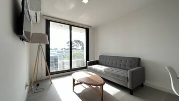 Uma sala de estar moderna com um sofá cinzento, uma mesa de centro de madeira e um abajur.