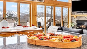 Una mesa de comedor de madera con una bandeja de frutas, un cartel que dice "SUNDAY RIVER" y una chimenea de piedra.