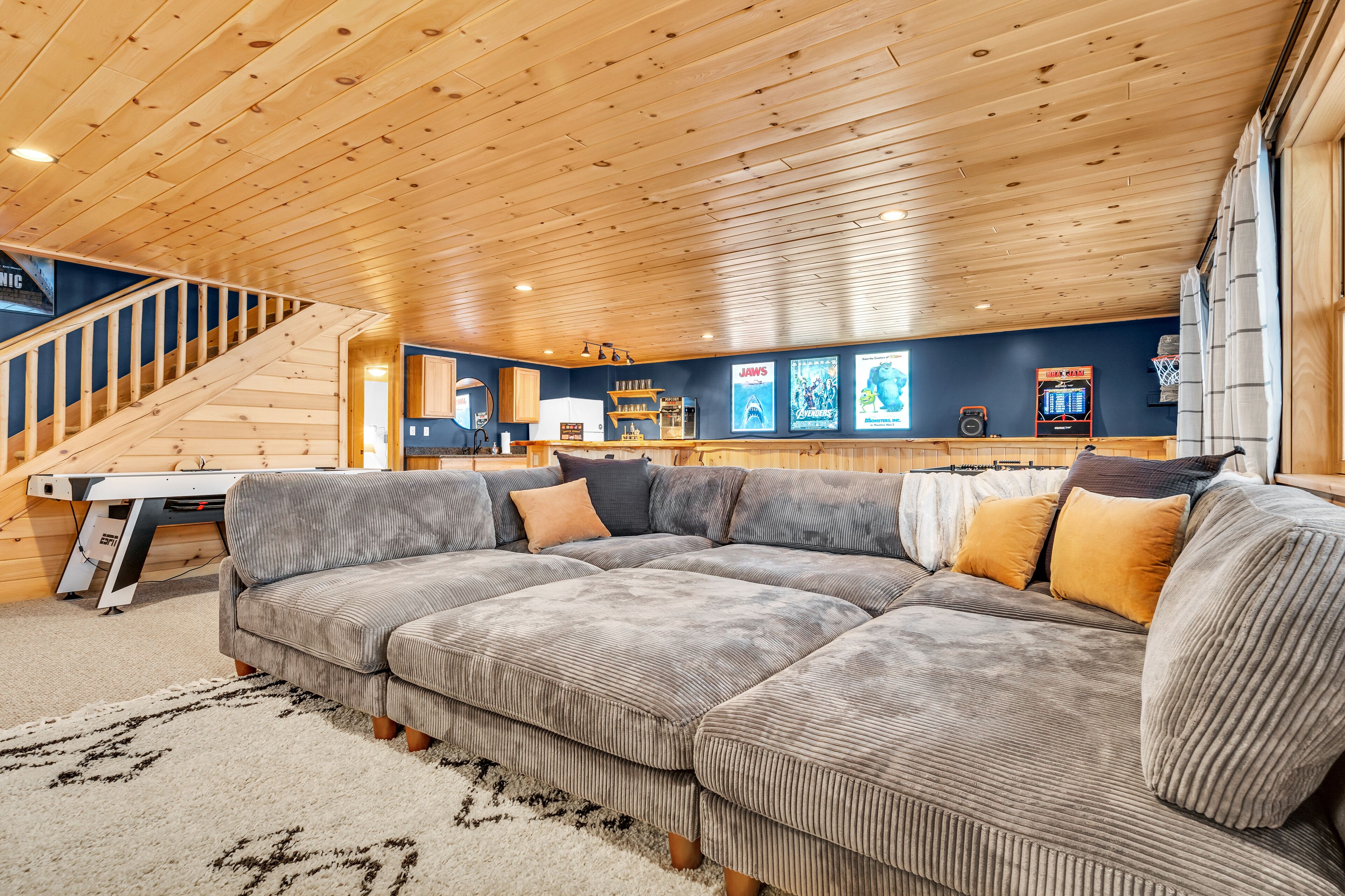 A spacious living area with a large sectional sofa, a wooden staircase, and a basketball hoop.