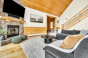 A cozy living room with a stone fireplace, a large flat-screen TV, a gray sofa with a throw blanket, and a wooden ceiling. - Sleeps 16+ Hot Tub with Mountain View - 3Min to Sunday River Ski - Game Room

 (Newry)